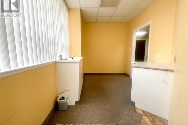 Empty room with beige walls, carpet flooring, and windows providing natural light - 110-112 Third Street W, Cochrane