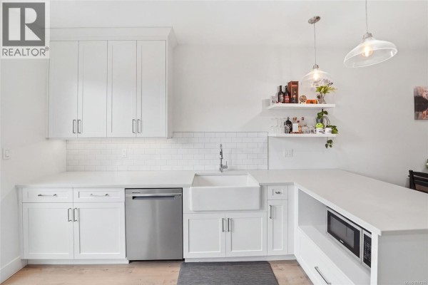 Modern white kitchen with a farmhouse sink, stainless steel dishwasher, and subway tile backsplash. - 110 3003 Keystone Dr, Duncan