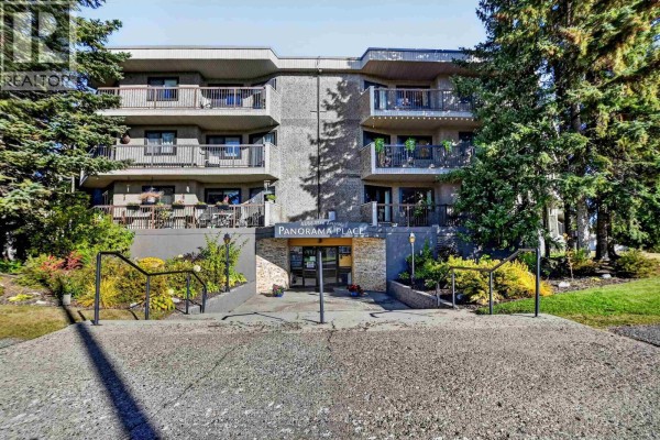 Front exterior of the Panorama Place apartment building with balconies and trees. - 110 4288 15th Avenue, Prince George