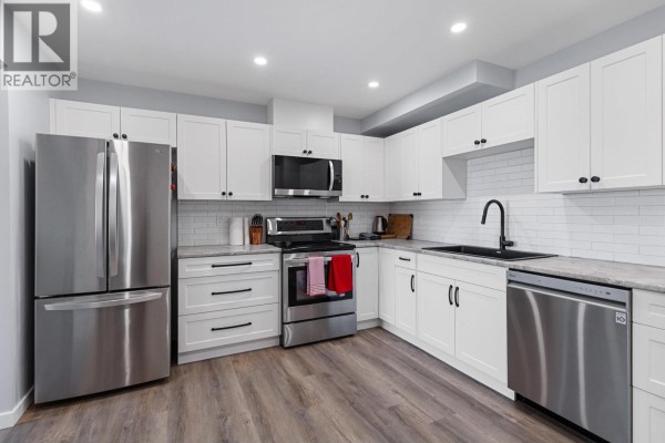 Bright white kitchen with stainless steel appliances, grey countertops, white subway tile backsplash, and dark fixtures. - 110 455 Killoren Crescent, Prince George