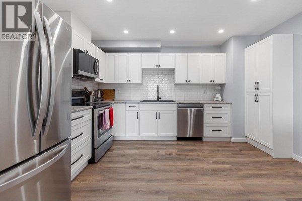 Spacious white kitchen with stainless steel appliances, ample white cabinetry, and wood-look laminate flooring. - 110 455 Killoren Crescent, Prince George