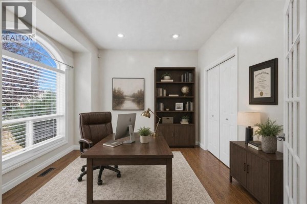 Office with a desk, chair, bookshelf, and large arched window with blinds. - 110 Ainsworth Crescent, Red Deer
