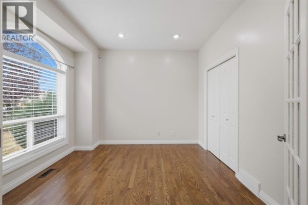 Empty room with wood floors, white walls, closet doors, and large arched window. - 110 Ainsworth Crescent, Red Deer