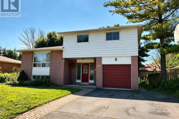 Side view of a two-story house with brick and white siding, red garage door, and green lawn. - 110 College Crescent, Barrie