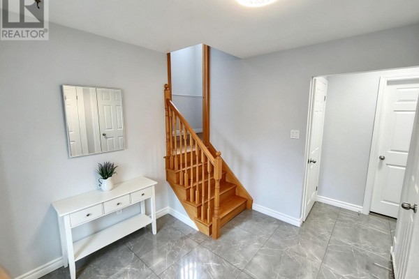 Foyer with light grey walls, a wooden staircase, white console table, and grey tiled floor. - 110 College Crescent, Barrie