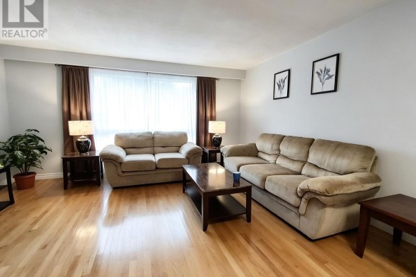 Living room with hardwood floors, two beige sofas, a coffee table, and large window with brown curtains. - 110 College Crescent, Barrie