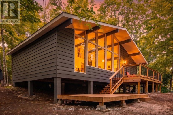 Interior view of the cottage showcasing the A-frame window wall illuminated at dusk. - 110 Fire Route 367, Trent Lakes