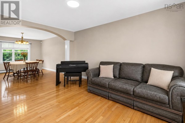 Living room with a dark grey sofa, digital piano, and dining area visible through an arched doorway. - 110 Gleneagles Drive, Hammonds Plains