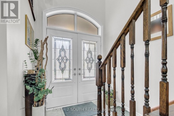 Double white entry doors with stained glass windows and a wooden staircase inside. - 110 Grand Trunk Avenue, Vaughan