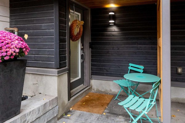 Entrance to townhouse with dark wood siding, teal chairs, and pink flowers. - 110 Greenfield Avenue, Ottawa