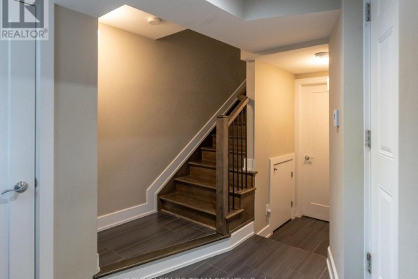 Interior hallway with dark wood staircase, grey tile floors, and white doors. - 110 Greenfield Avenue, Ottawa