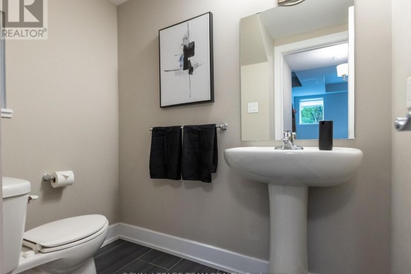 Powder room with a white pedestal sink, toilet, and beige walls. - 110 Greenfield Avenue, Ottawa