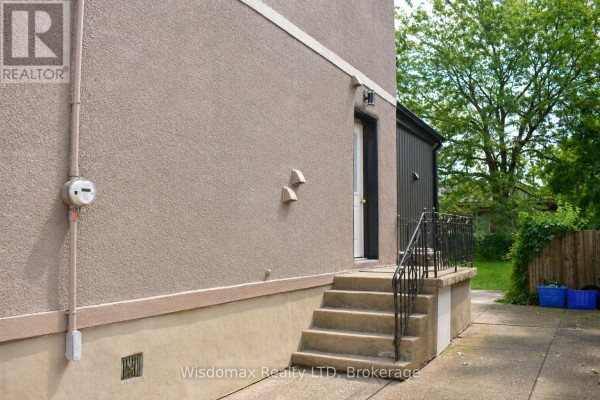 Side exterior of a house with a concrete foundation and steps leading to a back door. - 110 Queen Street S, Thorold
