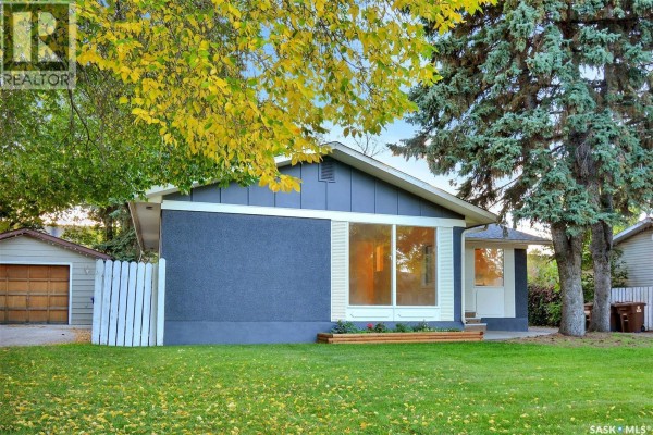 Side view of the bungalow with a garage, white fence, and autumn foliage. - 110 Spinks Drive, Saskatoon