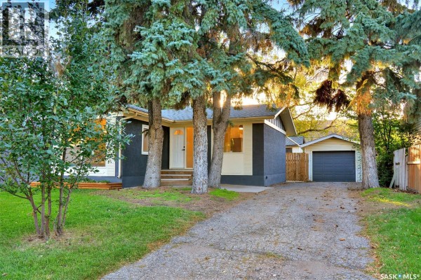 View of the house entrance and driveway surrounded by mature trees and greenery. - 110 Spinks Drive, Saskatoon