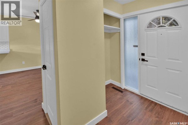 Interior entryway with a white front door, glass sidelight, closet shelf, and wood-look flooring. - 110 Spinks Drive, Saskatoon