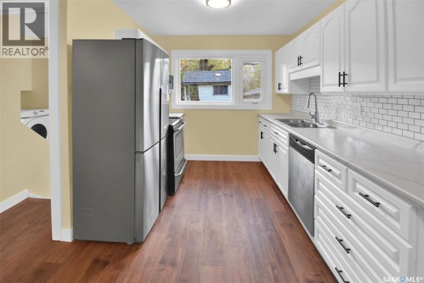 Kitchen with white cabinets, subway tile backsplash, stainless steel appliances, and wood-look flooring. - 110 Spinks Drive, Saskatoon