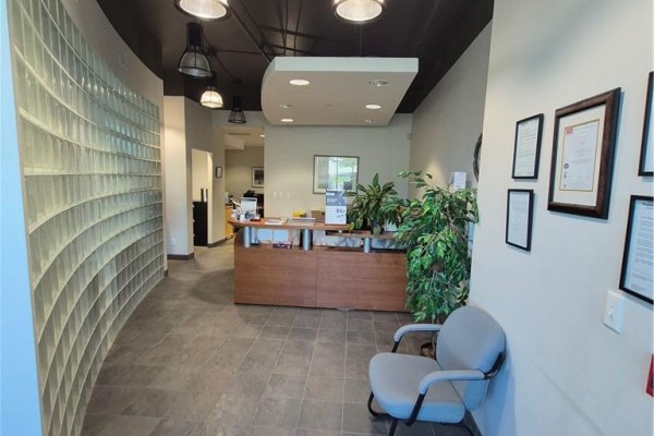 Reception area with a wooden desk, grey tiled floor, a grey chair, and a curved glass block wall. - 1100 South Service Road Unit# 114, Stoney Creek