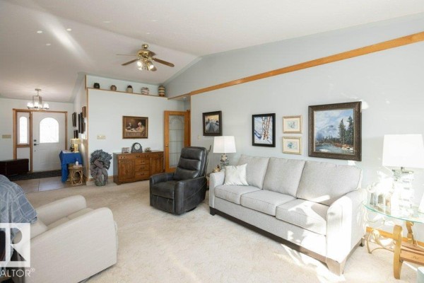 Living room with beige carpet, light blue walls, furniture, and entryway visible in the background. - 11007 108 Av, Westlock