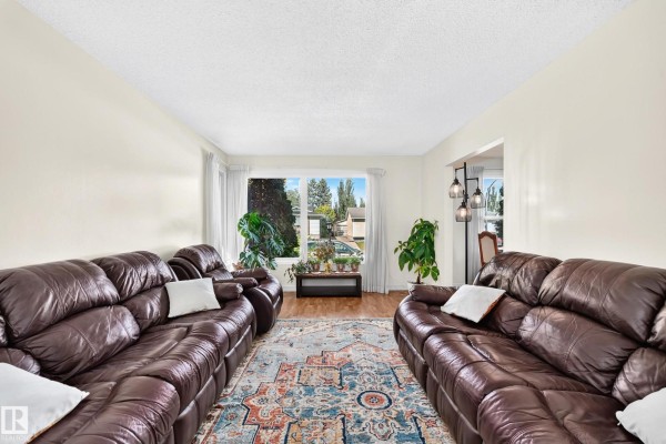 Living room featuring two large brown leather sofas, a colorful rug, and a large window. - 11007 173a Av Nw, Edmonton