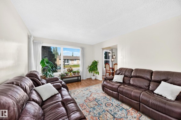 Living room with two brown leather sofas facing a wide window with a view of the neighborhood. - 11007 173a Av Nw, Edmonton