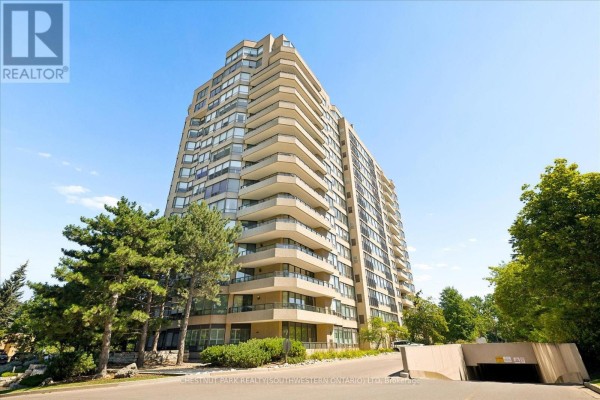 Exterior of a tall, beige apartment building with numerous balconies under a clear blue sky. - 1101 - 4 Willow Street, Waterloo