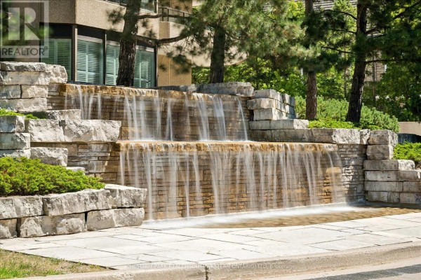 Multi-tiered stone waterfall feature with water flowing down stone blocks surrounded by greenery. - 1101 - 4 Willow Street, Waterloo