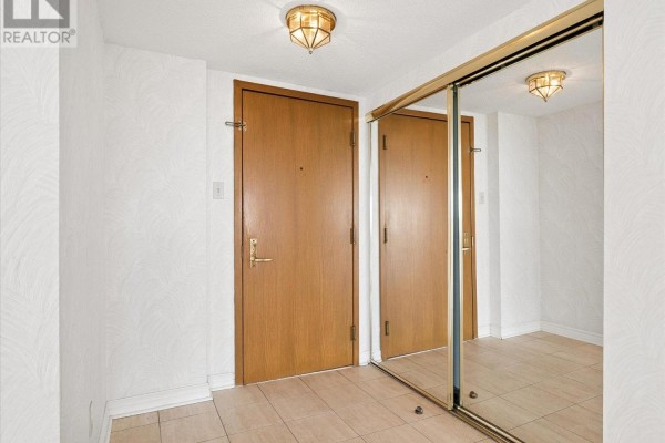 Apartment entryway with beige tiled floor, white textured walls, and mirrored closet doors. - 1101 - 4 Willow Street, Waterloo