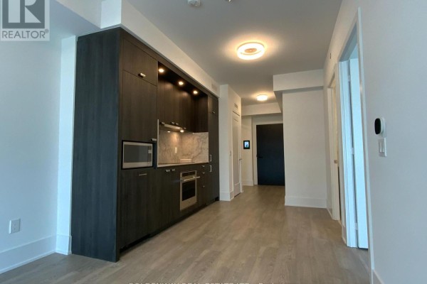View of the apartment's kitchen and hallway, showing dark cabinets and light wood flooring. - 1101 - 470 Front Street W, Toronto