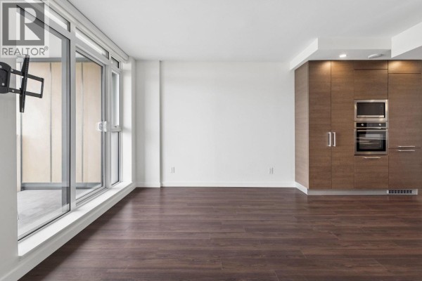 Empty living room with dark wood floors, large windows, and built-in kitchen cabinets. - 1101 285 E 10th Avenue, Vancouver