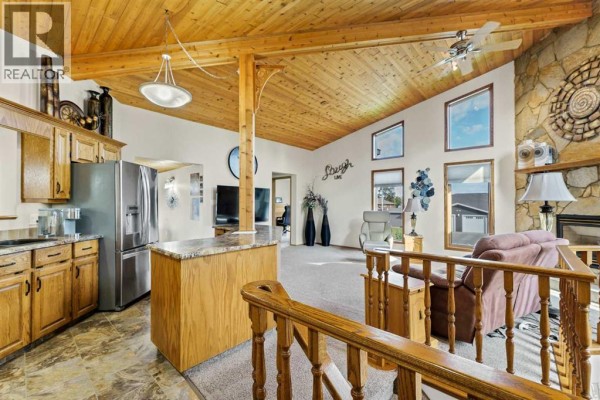 Open concept living area with vaulted wood ceiling, stone fireplace, and view of kitchen. - 1101 Centre Street, Bow Island