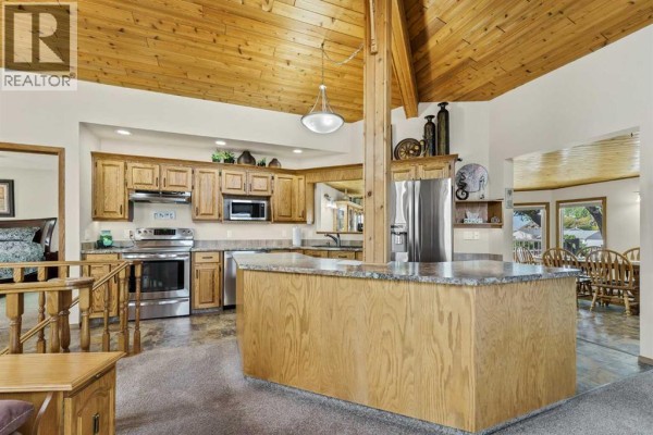 View of the open kitchen with wood cabinets, island, and dining area in background. - 1101 Centre Street, Bow Island