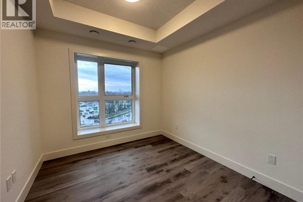 Empty room with wood-look flooring, white trim, and a large window showing an urban streetscape. - 1101 Lackner Place Unit# 411, Kitchener
