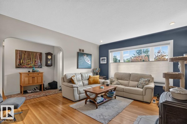 Living room with beige sofas, wood floors, and an arched entryway to another room. - 11010 110 Av Nw, Edmonton