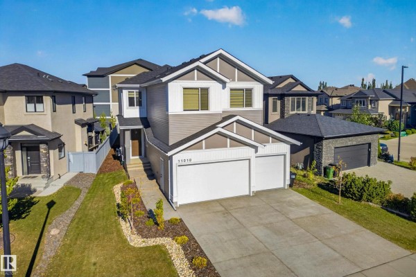 Front exterior view of a two-story house with a gray and white facade, a paved driveway, and a garage. - 11010 174a Av Nw, Edmonton
