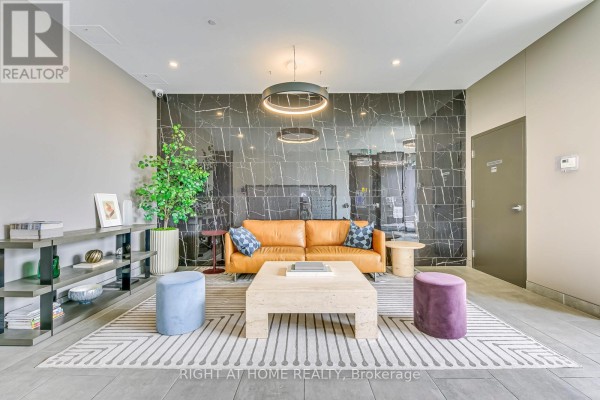 Lobby seating area with orange sofa, decorative pillows, and patterned rug. - 1102 - 100 Garment Street, Kitchener