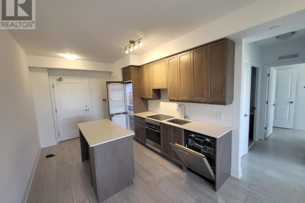 Wide view of a kitchen with grey cabinets, island, stainless steel appliances, and open doors. - 1102 - 30 Elm Drive W, Mississauga