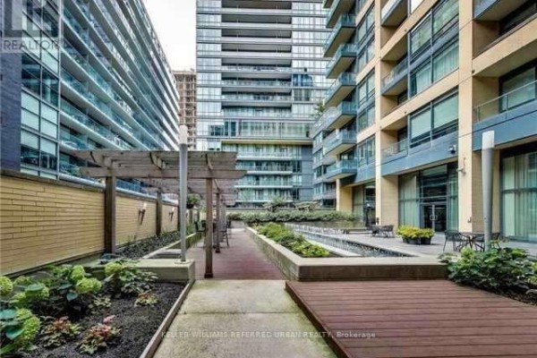 Outdoor courtyard with wooden decks, water features, planters, and seating areas between buildings. - 1102 - 438 King Street W, Toronto