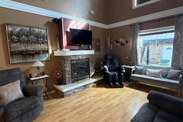 Living room with a stone fireplace, mounted TV, massage chair, and a grey sofa. - 1102 Alfred Street, Cochin