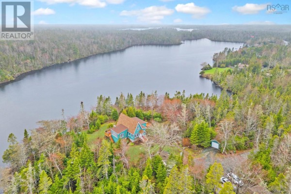 Expansive aerial view of a teal house nestled amongst trees on the shore of a wide lake. - 11028 Highway 7, Lake Charlotte