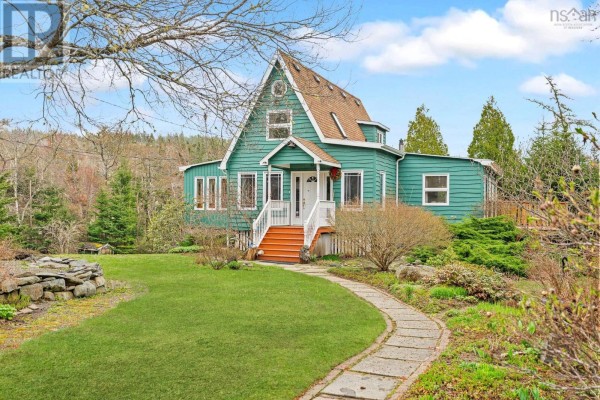 Front view of a teal house with a stone pathway, grassy lawn, and mature trees. - 11028 Highway 7, Lake Charlotte