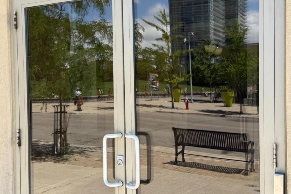 Reflection of trees and buildings on the glass doors of the building. - 1103 - 350 Princess Royal Drive, Mississauga