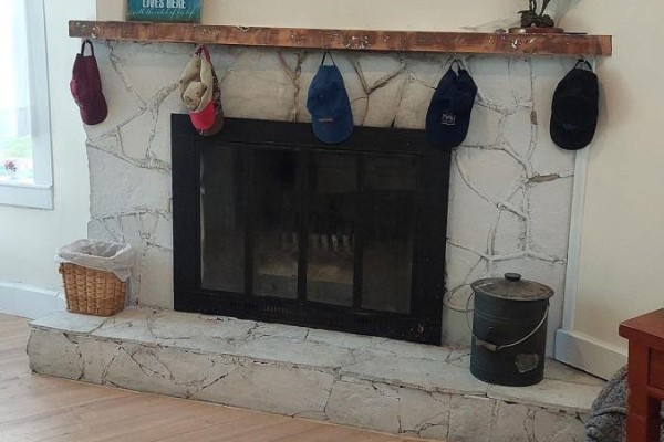 Stone-faced fireplace with glass doors, wooden mantelpiece with stockings and hats hanging. - 1103 Cronk Road, Frontenac
