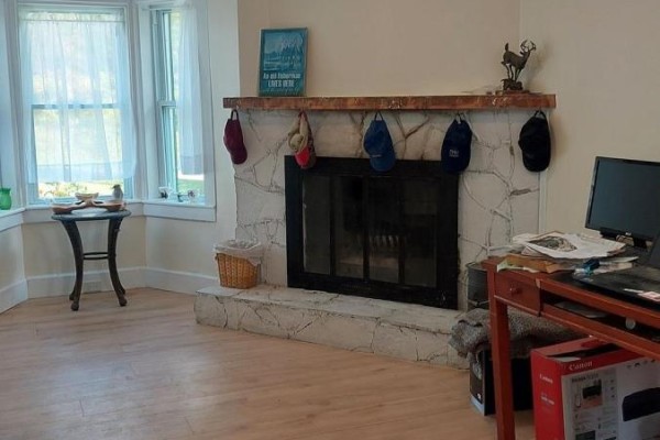 Living room with fireplace, bay window with white curtains, desk with computer and printer. - 1103 Cronk Road, Frontenac