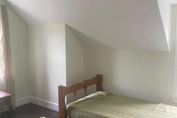 Bedroom with sloped ceiling, wooden bed frame with green blanket, pale green walls. - 1103 Cronk Road, Frontenac