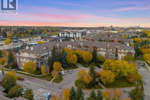 Aerial view of apartment complex with autumn trees and distant cityscape. - 1104, 1104 Lake Fraser Court Se, Calgary