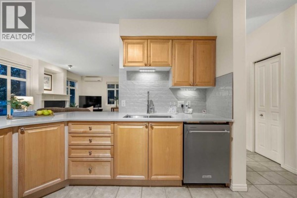 Kitchenette with light wood cabinets, white quartz countertops, and stainless steel dishwasher. - 1104, 1104 Lake Fraser Court Se, Calgary
