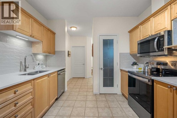 Kitchen with light wood cabinets, stainless steel appliances, and tiled floor. - 1104, 1104 Lake Fraser Court Se, Calgary