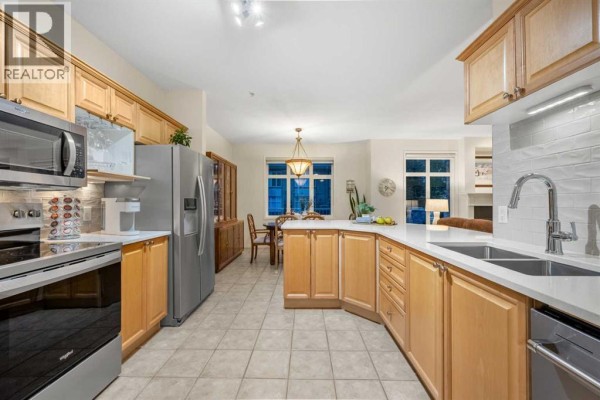 Spacious kitchen with light wood cabinets, stainless steel appliances, and dining area view. - 1104, 1104 Lake Fraser Court Se, Calgary