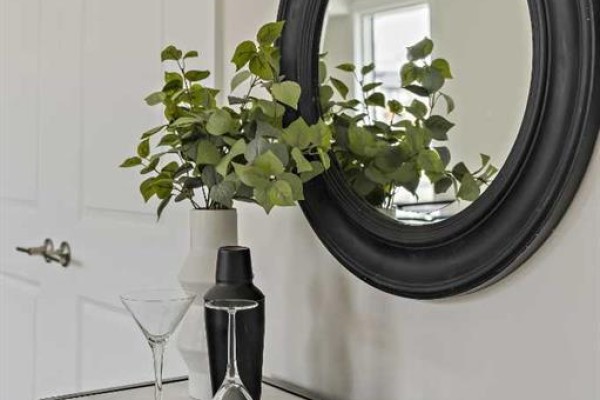 A decorative vignette with a large oval black mirror, green plant in a white vase, and cocktail glasses. - 1104, 60 Howse Lane, Calgary